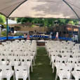 An outdoor ceremony set up with white plastic stackable chairs and a canopy.