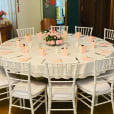A round table with white Tiffany chairs and pink tablecloths.