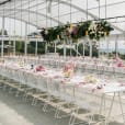 An outdoor wedding reception set up with white tables and pink flowers, featuring white wire chairs.