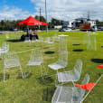 A group of white chairs, specifically the White Wire Chairs, set up on a grassy field.