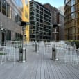 A white patio with chairs and tables in the middle of a city, featuring White Wire Stool seating options.