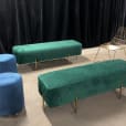 An emerald green velvet bench and two blue stools in a room.