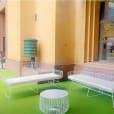 A white table and chairs on a green carpet in front of a building available for White Arrow 3 Seater Lounge Hire.