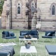 A set of outdoor furniture in front of a church, featuring wire arm chairs and navy blue velvet cushions.