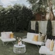 A white wire sofa lounge set with white velvet cushions in a backyard.