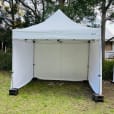 A white 3mx3m pop up tent is set up in a grassy area.