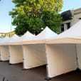 A row of 3mx3m pop up marquees with walls on 3 sides, lined up on a street.