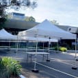 A group of 3mx3m pop up marquees with white roofs set up in front of a building.