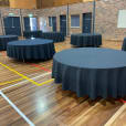 Tables and chairs, including round timber banquet tables, are set up in a gymnasium.