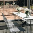 A white hairpin high bar table set up with white chairs and flowers.