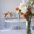 A white table with orange and white flowers on it available for White Wire Cocktail Table Hire.