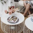 A white wire coffee table adorned with flowers, available for hire.