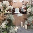 A wedding cake decorated with flowers, candles, and a clear square acrylic plinth.