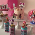 A pink cake with dolls and balloons on a white metal cake stand.