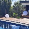 A wooden deck with a pool in the background featuring a mesmerizing Glow Sphere Hire - 60cm.