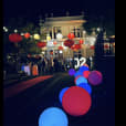 A group of people are walking down a street at night, carrying Glow Spheres measuring 50cm.