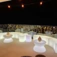 A balcony bar with white glowing lights and stools for hire.