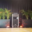 A stage with a speaker and plants in front of it, featuring Pkg 2: Jukebox & Karaoke Hire.