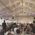 A group of people sitting at tables in a tent adorned with Festoon Light Hire.