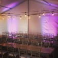 A tent with tables and chairs set up with purple festoon lighting.