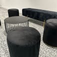 A black wire coffee table next to black ottoman stools and a lounge
