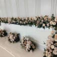 White gloss bridal table featuring elegant floral décor in soft neutral tones, with roses, orchids, and greenery styled for a modern wedding reception.