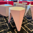 Close-up of a white Puzzle Stool with angular legs on a patterned black carpet, surrounded by cube ottomans and a small round table in a bright event setting.