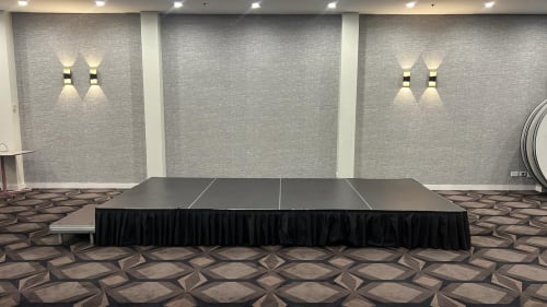Low-rise modular event stage with black skirting set up in a function room with patterned carpet and wall lighting