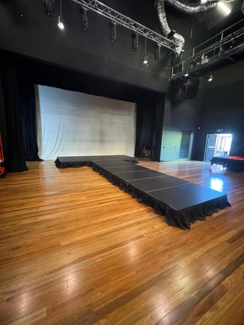 A black stage with a small runway on a wooden floor