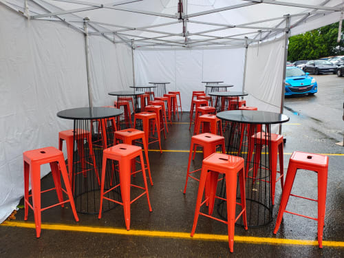 Black wire tables and red Tolix stools under a marquee