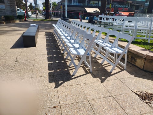 Lots of white plastic chairs set up on the pavement ready for use