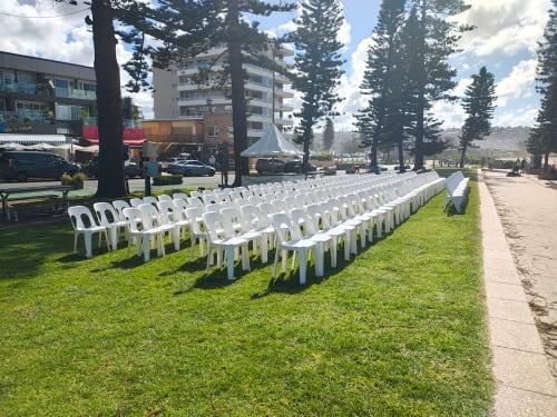 Hundreds of white plastic chairs set up for an outdoor event next to the beach