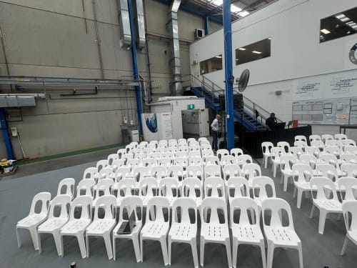 Scores of white stackable chairs hired for a conference in an industrial plant