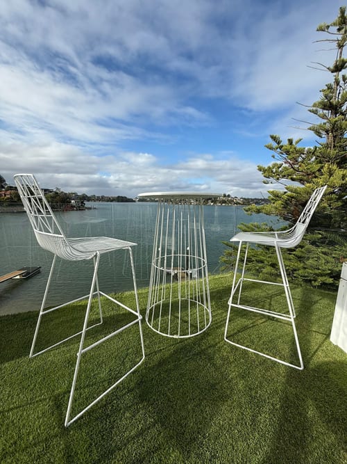White wire table and stools hired and placed on grass in front of water