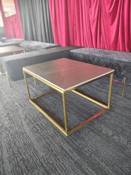 A brass-framed square coffee table in front of some red drapes