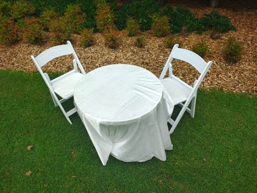 Two white plastic folding chairs next to a table on the grass