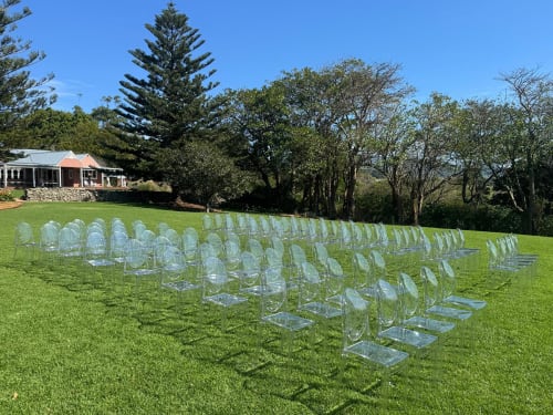 Lots of clear plastic Victorian ghost chairs set up for a wedding in a park