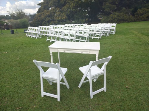 Lots of white plastic folding chairs and a signing table ready for a wedding in an outdoor park