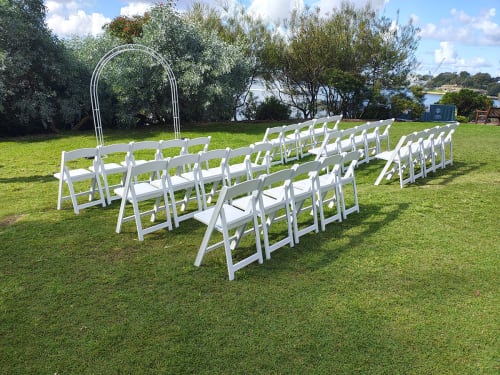 Lots of white plastic chairs set up in a park ready for a wedding