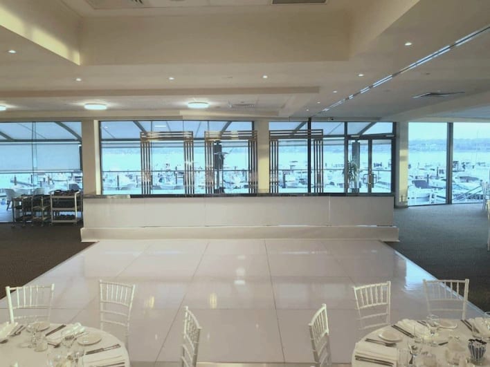 A room with white tables and chairs and a view of the ocean.
