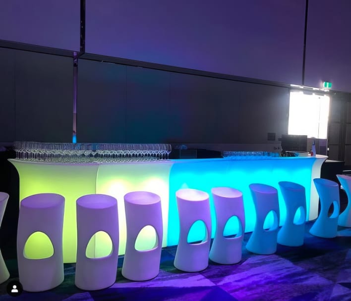 A bar set up with colorful lights and stools.