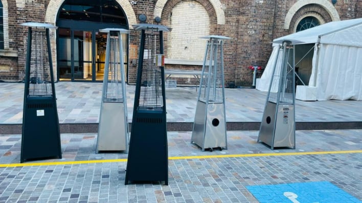 A group of outdoor heaters in front of a brick building.