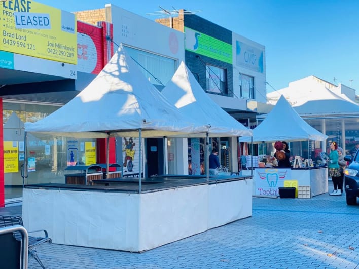 A street market with white tents and parked cars.