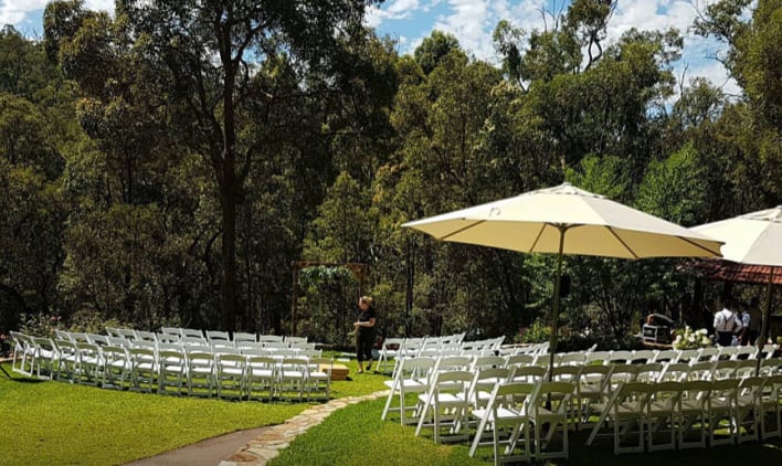 An outdoor wedding ceremony with white chairs and umbrellas.