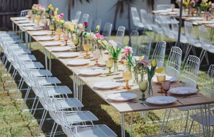 A long table set up with white chairs and flowers.