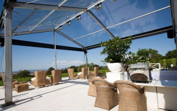 A clear tent with wicker furniture and a grill.