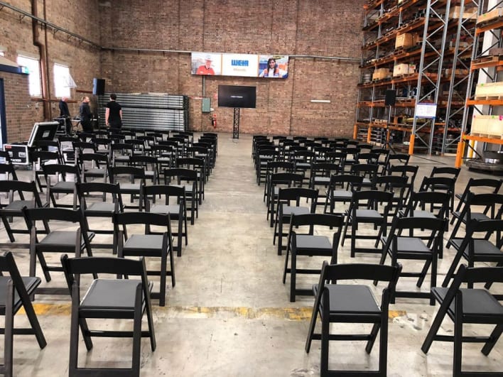 A large warehouse with rows of black folding chairs.