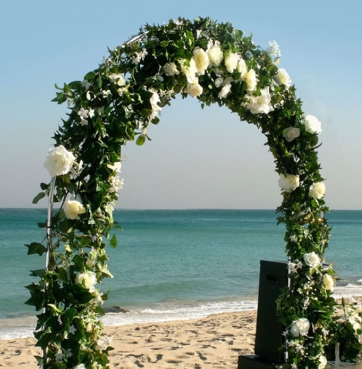 A wedding arch decorated with white flowers on the beach.