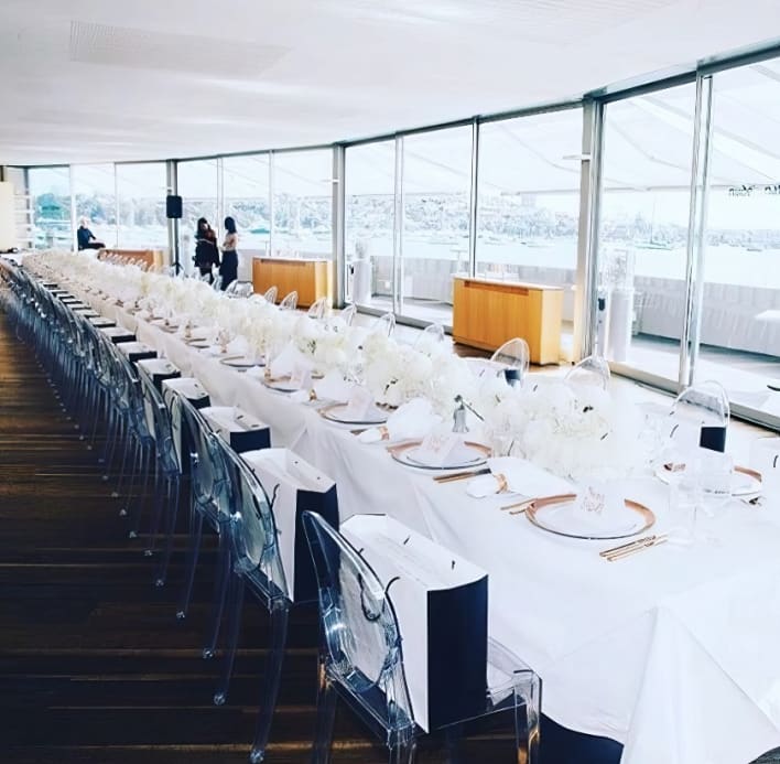 A long table with white chairs and a view of the water.
