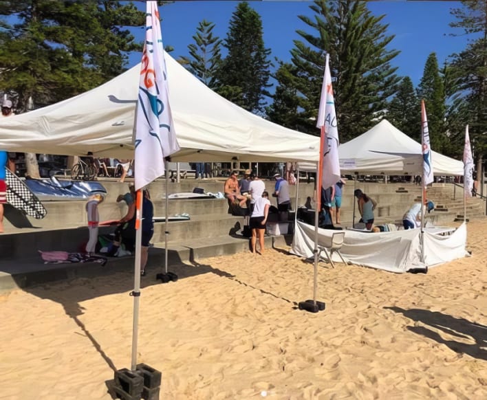 A group of people standing under tents on the beach.